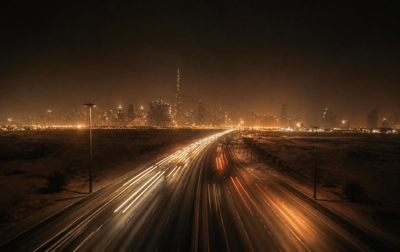 Night highway with light trails toward a distant skyline
